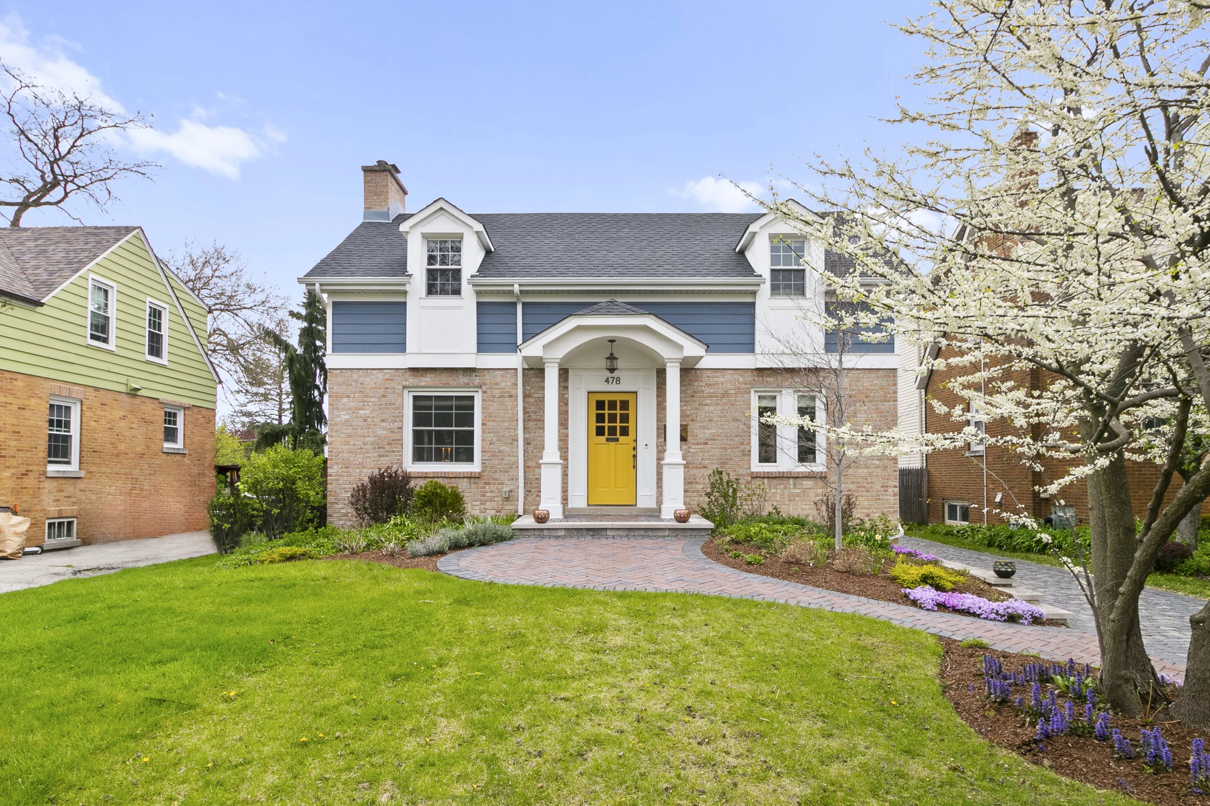 Two-story home with a yellow front door, landscaped lawn, and flowering tree