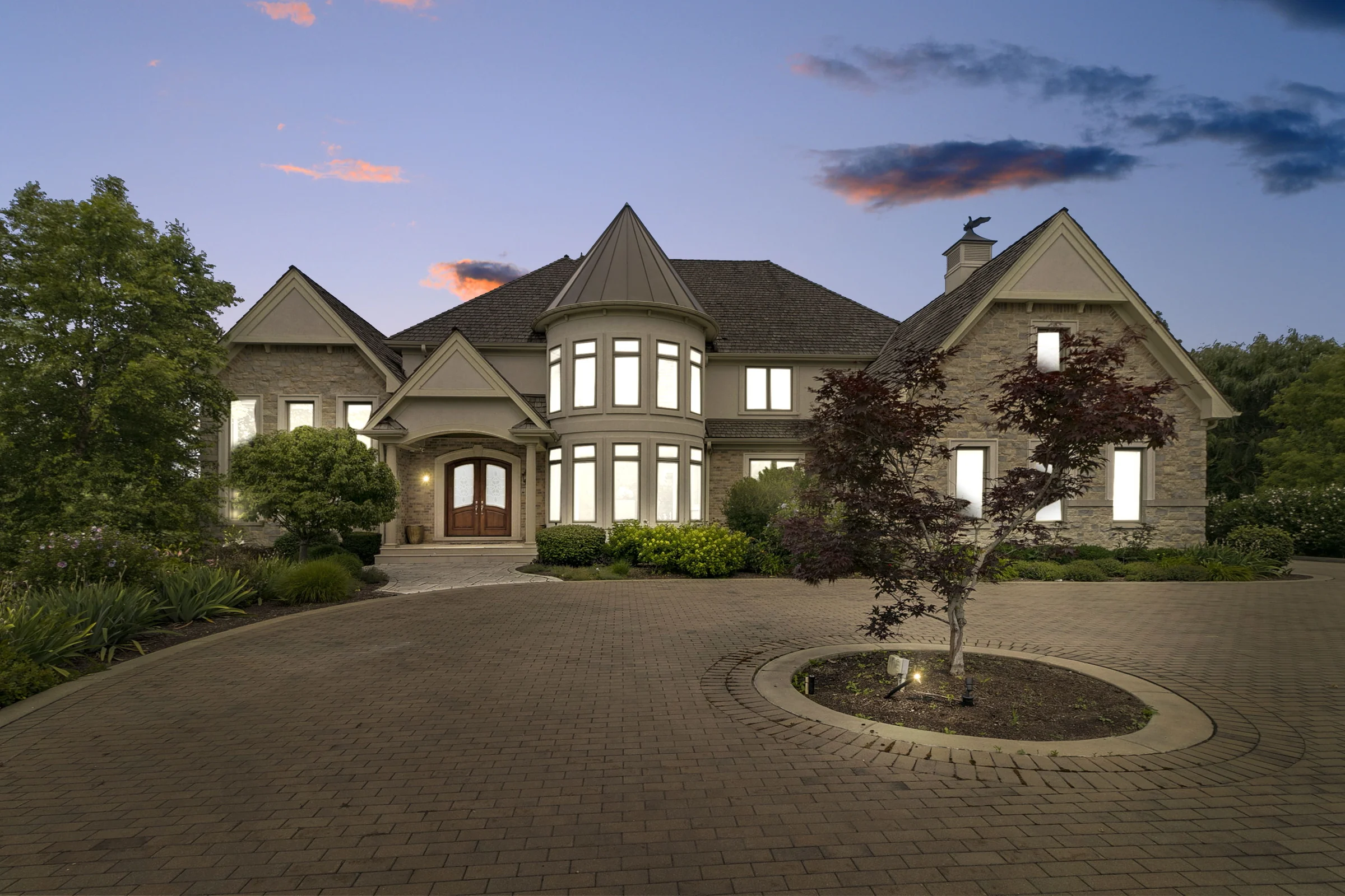 Home at twilight with illuminated windows and a circular paved driveway